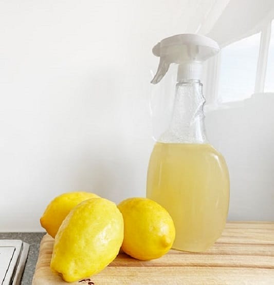 Lemons beside a spray bottle of green cleaning solution.